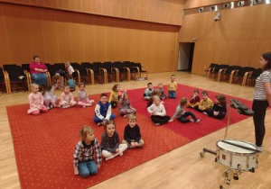 dzieci siedzą na dywanie i słuchają opowieści o instumentach perkusyjnych