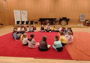 dzieci siedzą na dywanie i słuchają opowieści o instumentach perkusyjnych
