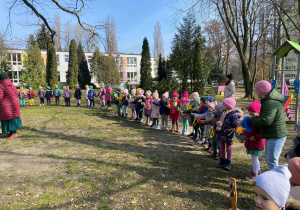 Dzieci stojąc w kole w przedszkolnym ogrodzie świętują pierwszy dzień wiosny