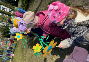 Dzieci stoją z papierowymi kwiatami w przedszkolny ogrodzie