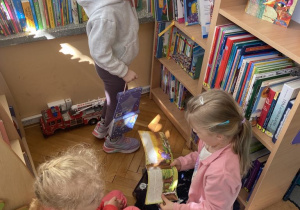 Dziewczynki przeglądają książeczki zgromadzone na bibliotecznych regałach