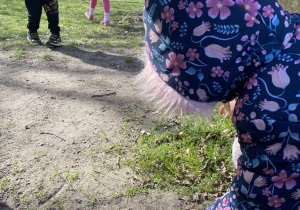Dziewczynka szuka pisanek ukrytych w przedszkolnym ogrodzie