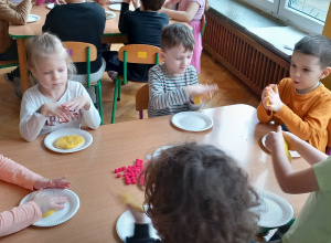 Dzieci przy stole gniotą masę solną tworząc placki pizzy