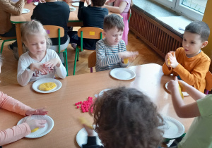 Dzieci przy stole gniotą masę solną tworząc placki pizzy