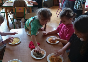 Dzieci ozdabiają swoje pizze wybranymi przyprawami