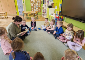 Dzieci siedzą w kole i słuchają bajek czytanych przez rodzica.