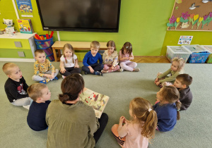 Dzieci siedzą w kole i słuchają bajek czytanych przez rodzica.