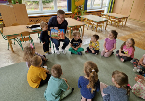 Dzieci siedzą w kole i słuchają bajek czytanych przez rodzica.