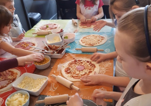 Dzieci układają dodatki na cieście do pizzy