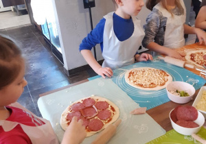 Dzieci układają dodatki na cieście do pizzy