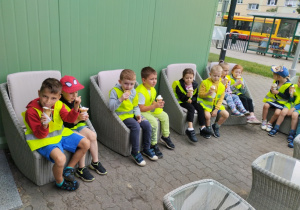 Dzieci jedzące lody siedzą przed lodziarnią.