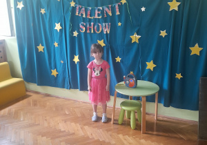 Dziewczynka stoi obok stolika i śpiewa piosenkę