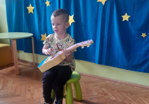 Chłopiec siedzi na stołeczku i gra na gitarze