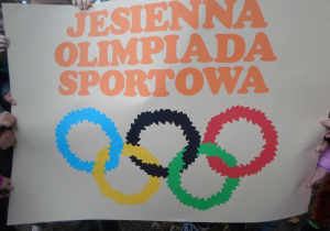 Dzieci trzymają plakat jesiennej olimpiady sportowej