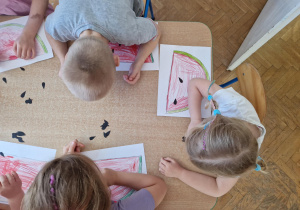 dzieci przy użyciu słomki zasysają pestki i przenoszą je na sylwetę pokolorowanego arbuza