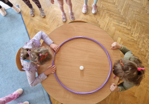 dzieci w parach na  przeciwko siebie wprowadzają w ruch piłeczkę na zmianę w obrębie hula hop.