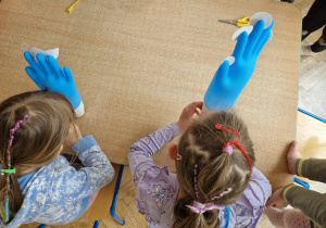 dzieci nadmuchują rękawiczkę naciągniętą na kubeczek papierowy przy użyciu słomki.