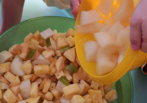 Dziewczynka wsypuje melony do miski z innymi owocami