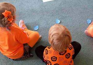 Dzieci siedzą w siadzie skrzyżnym i mają położone przed sobą krople deszczu