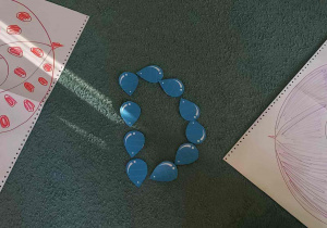 Na dywanie leżą kartony z narysowanymi parasolkami oraz literka D utworzona z kropelek