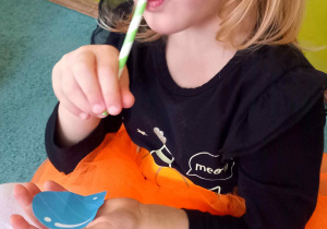 Dziewczynka trzyma sylwetę kropelki na dłoni i stara się zassać powietrze przez papierową słomkę