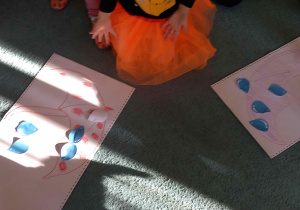 Na dywanie leżą parasolki a na nich poprzenoszone przez dzieci papierowe kropelki