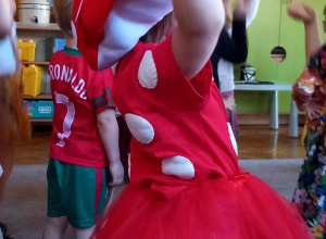 Dziewczynka przebrana za muchomorka ma uniesione dłonie i tańczy w rytm muzyki