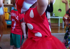 Dziewczynka przebrana za muchomorka ma uniesione dłonie i tańczy w rytm muzyki