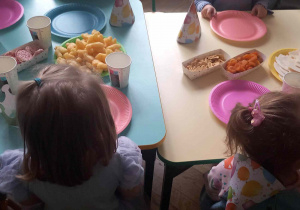 Dzieci siedzą przy stoliku i próbują przekąsek przygotowanych przez rodziców