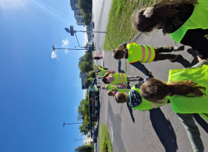 Dzieci stoją parami i przygotowują się do przejścia na drugą stronę jezdni