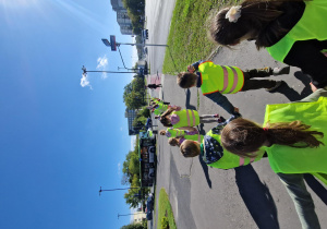 Dzieci stoją parami i przygotowują się do przejścia na drugą stronę jezdni