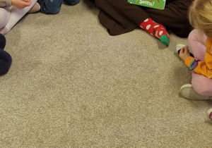 Dzieci siedzą na dywanie i słuchają bajki