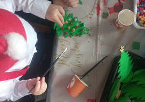 Chłopiec razem z mamą dekoruje drewnianą choinkę