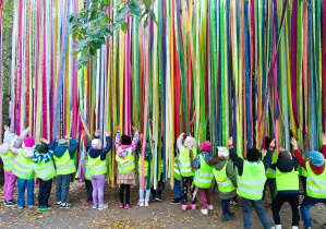 Dzieci bawią się kolorowymi wstążkami zawieszonymi nad ich głowami.