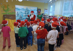 Dzieci rozmawiają ze Świętym Mikołajem niosącym worek z podarunkami.