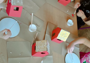 Dzieci przyklejają domek do podstawy.