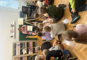 Dzieci siedzą przed prowadzącą zajęcia i słuchają czytanej przez nią bajki.