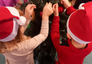 Dzieci zakładają plastikowe pierniczki i inne ozdoby na choinkę