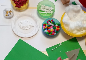 Dzieci metoda wydzieranki wyklejają choinkę a na stoliku leżą ozdoby