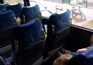 Dzieci siedzą w autokarze na fotelach i przypięte są pasami