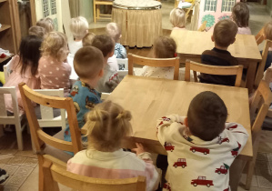 Dzieci siedzą na krzesełkach i z uwagą oglądają spektakl