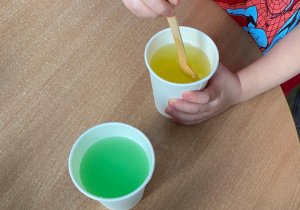 Chłopiec miesza łyżką wodę z żółtą farbą