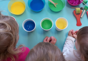 Na stole leżą pojemniki z zabarwionym śniegiem oraz kolorową wodą z pipetami