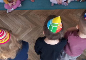 Dzieci tańczą w kolorowych czapeczkach przed dziećmi z pozostałych grup