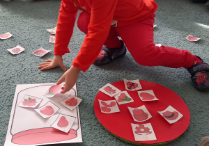 Dzieci wkładają do sloika z czerwona zakrętką ilustracje przedstawiające czerwone owoce i warzywa a na czerwonym kole pozostałe ilustracje