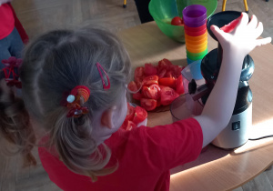 Dziewczynka wkłada pomidora do wyciskarki