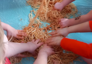 Dzieci stoją przy stoliku i bawią się kluskami