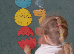 Dziewczynka układa obok czerwonego dinozaura jajko w odpowiednim kolorze