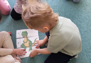 Chłopiec układa wspólnie z kolegami i koleżankami puzzle z wizerunkiem dinozaura