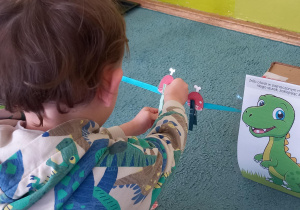 Chłopiec karmi dinozaura przypinając sylwety szynki klamerki na sznurek